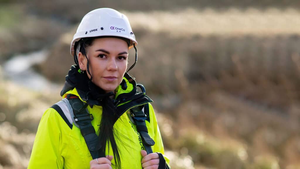 A young worker is looking at the camera with work clothing and a helmet on.