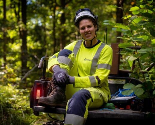 A OneCo worker is sitting in the back of a 4WD motorbike smiling at the camera.