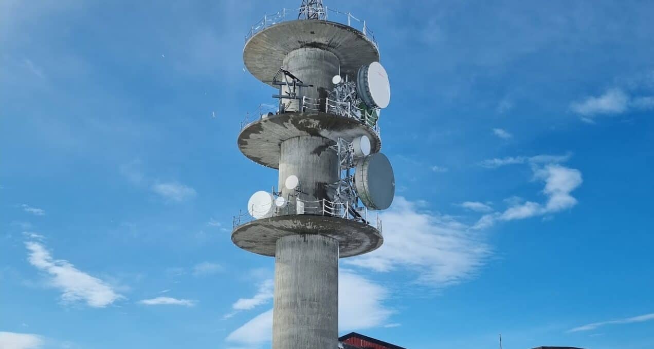 A worker is looking up at a large telecom tower in the snow.