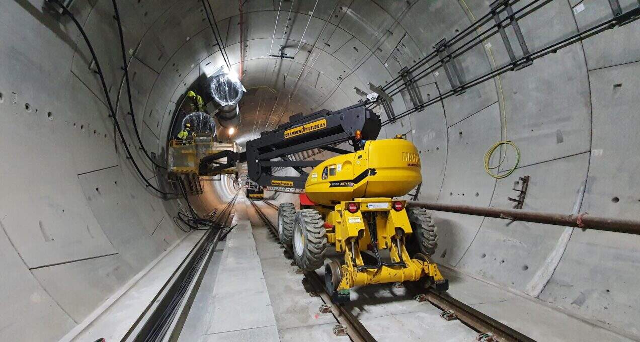 A lifter is in the forefront in a tunnel with two workers installing a fan system in the background.