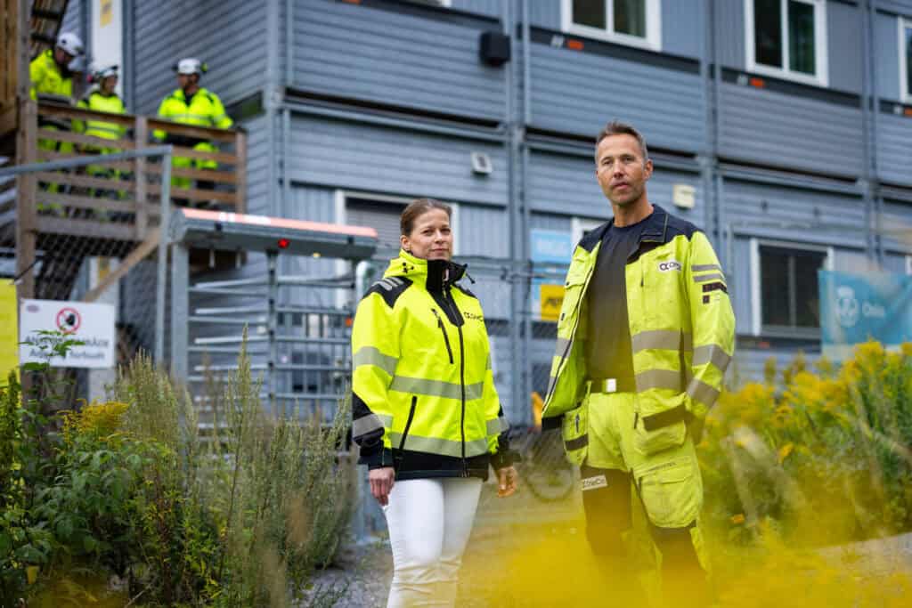 Bilde av Rannveig_Helen Ekløv og Kim Holteberg foran kontorene som brukes ved byggingen av det nye vannbehandlingsanlegget i Oslo. I bakgrunnen ser man noen av de som jobber på prosjektet.