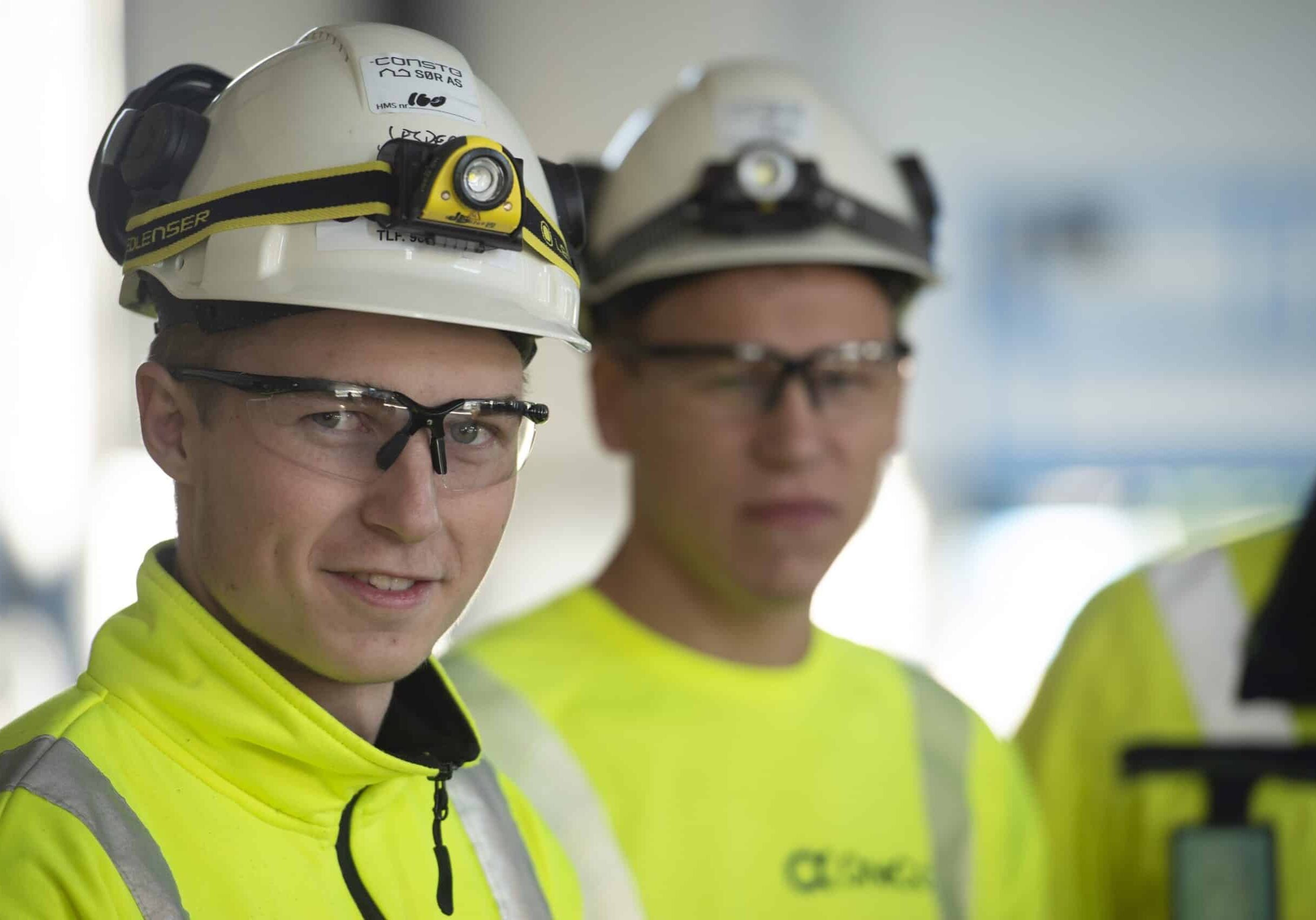 To OneCo-ansatte ser på kameraet, iført hjelmer og briller.